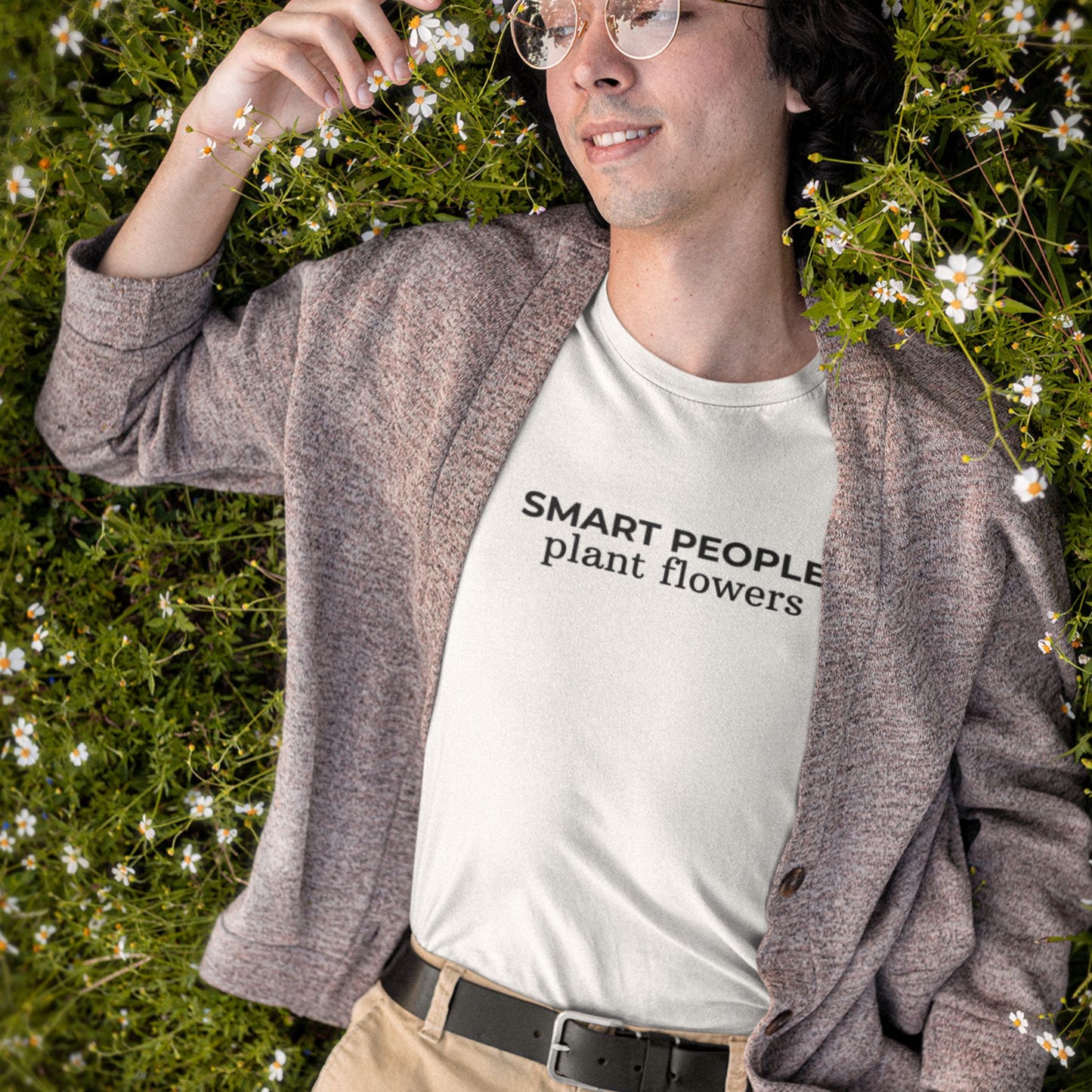 Person wearing a white t-shirt with 'SMART PEOPLE plant flowers' text, standing in a grassy area with flowers.