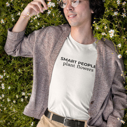 Person wearing a white t-shirt with 'SMART PEOPLE plant flowers' text, standing in a grassy area with flowers.